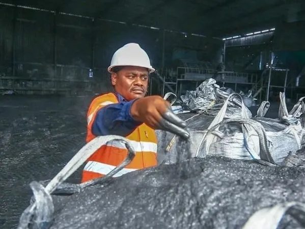 A mine worker in high-visibility clothing handling a bag of ore